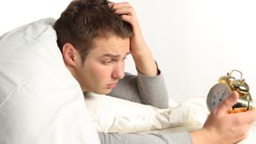 Tired Man Holding Alarm Clock in Bed